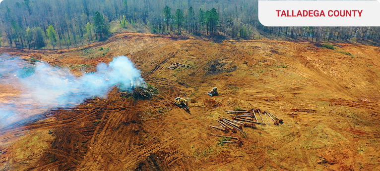 Aerial view of a cleared area with smoke and machinery in Talladega County