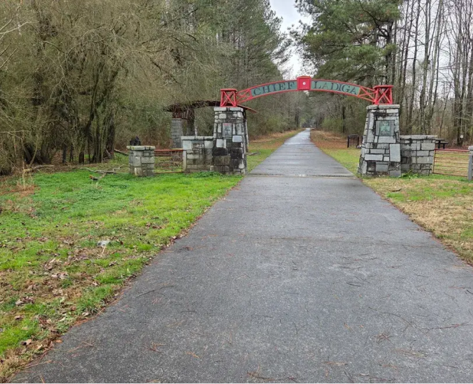 Stone entrance archway to a paved trail surrounded by trees