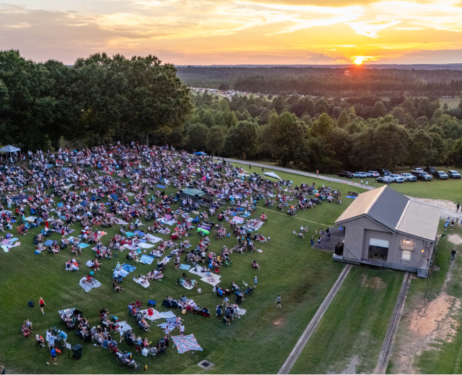 Large crowd enjoying an outdoor event at sunset on a grassy field