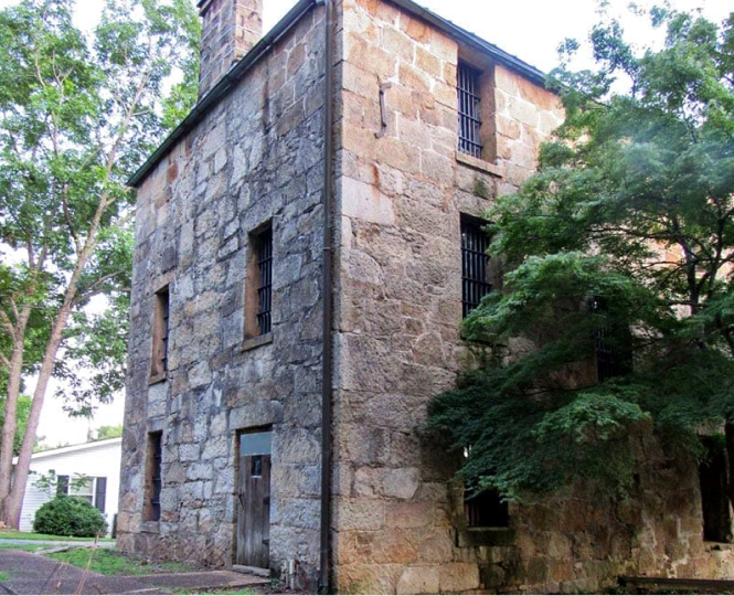 Stone building with barred windows and trees nearby